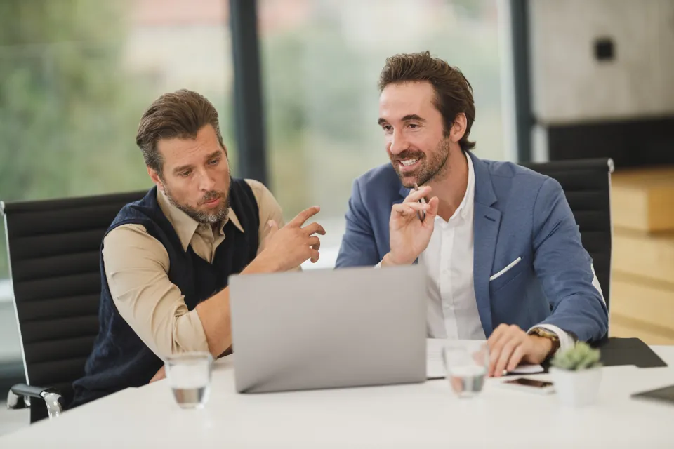 Duas pessoas conversando em uma mesa de reunião com um notebook