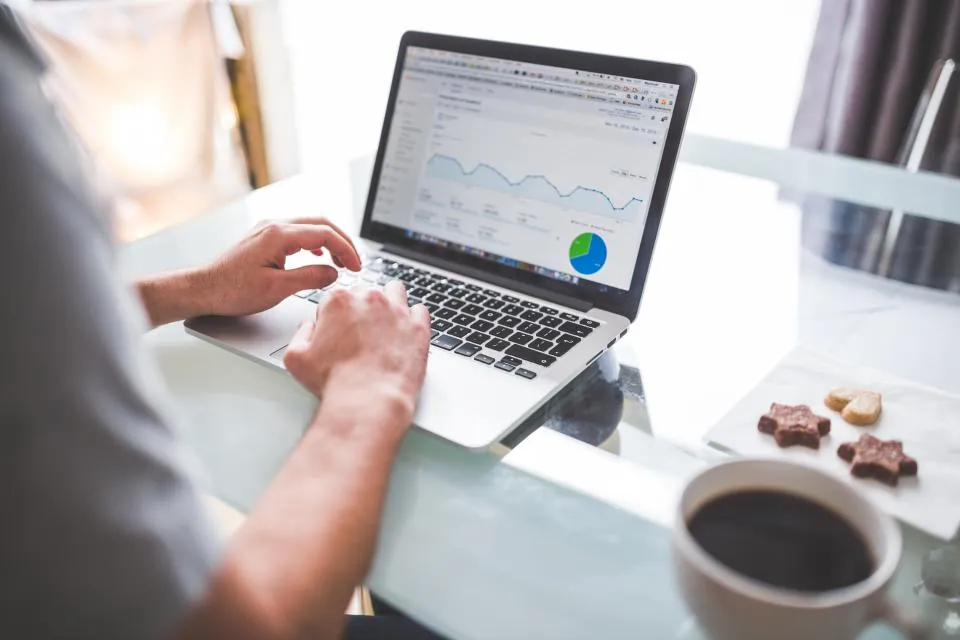 Notebook mostrando gráficos de um painel financeiro sobre uma mesa com uma xícara de café